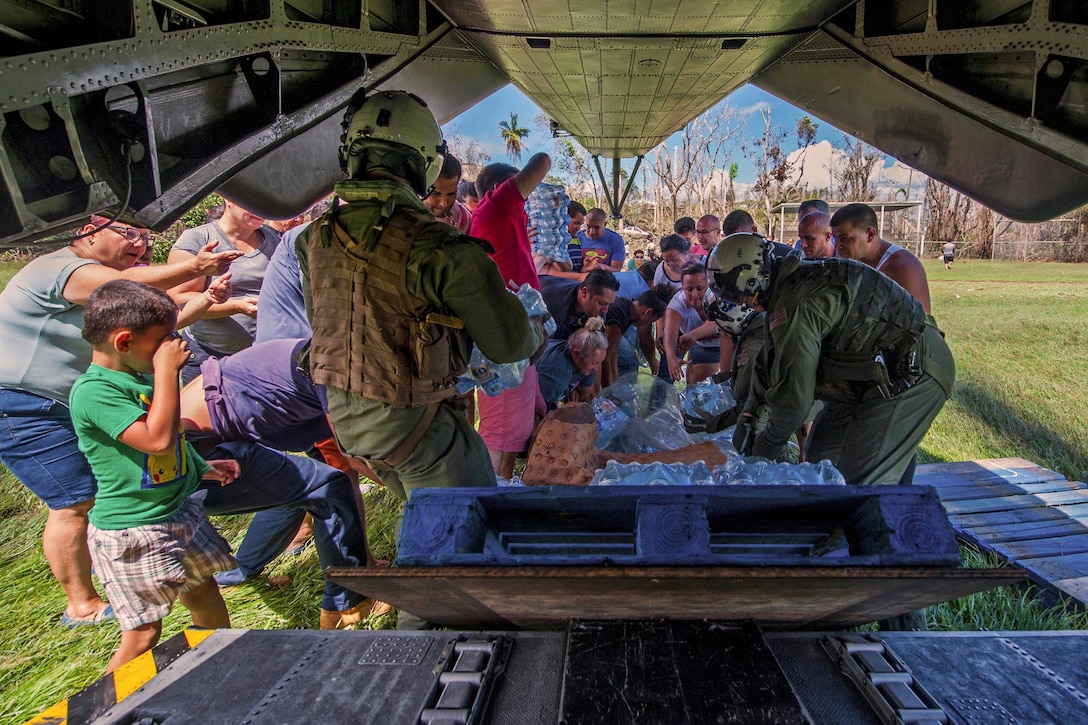 A group of people pick up water and other supplies behind an aircraft.