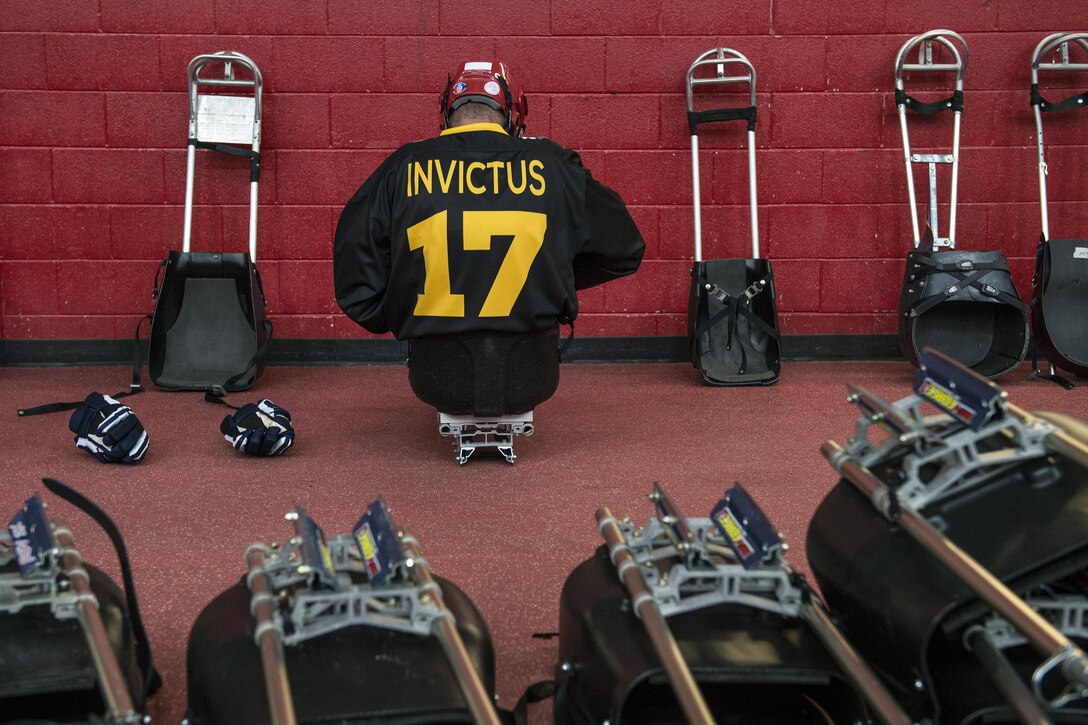 A sled hockey player faces a red wall as he prepares for a match.