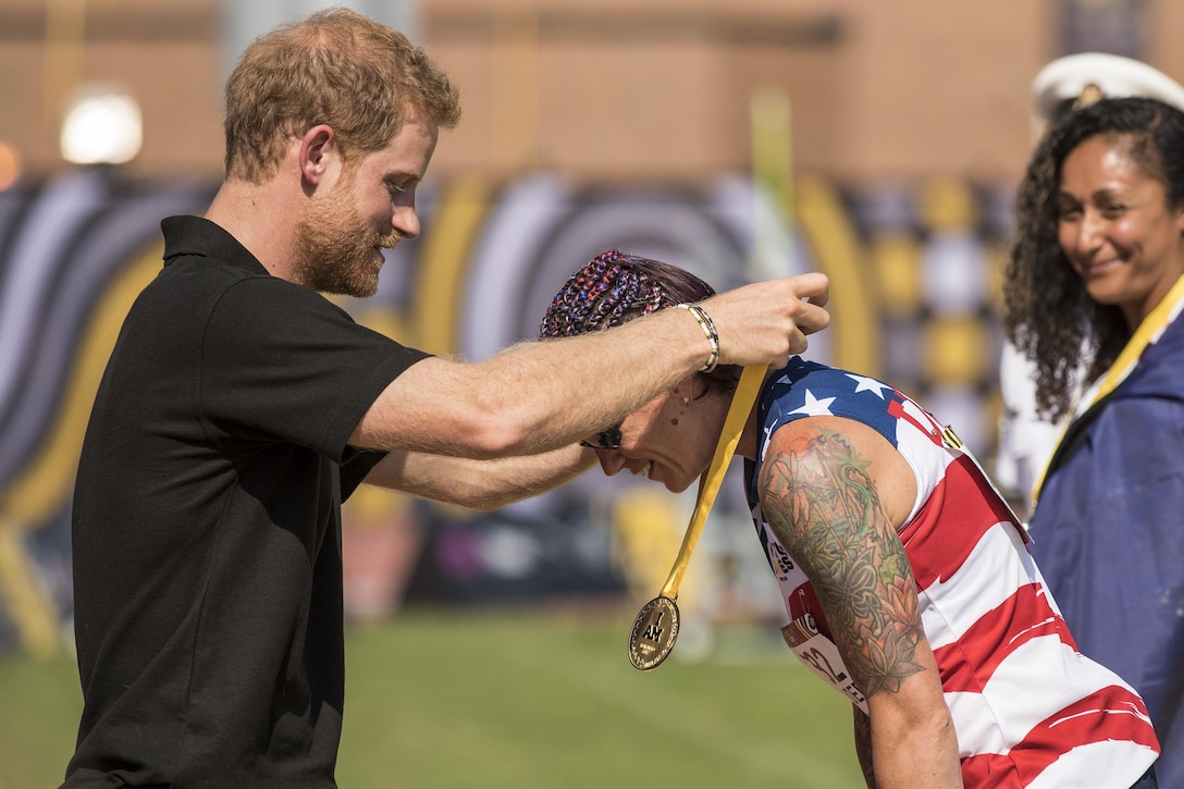 Prince Harry awards a medal to a Marine as she lowers her head.