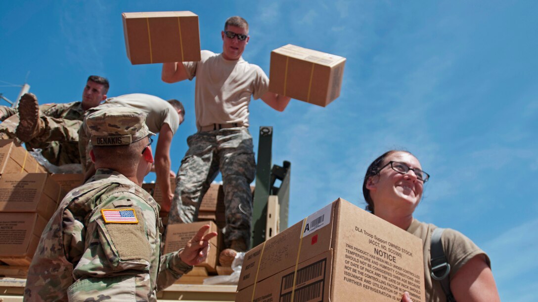 Soldiers unload boxes of supplies from a truck.