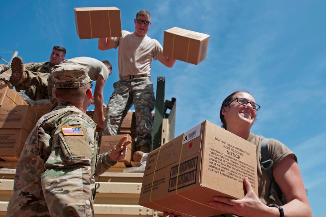 Soldiers unload boxes of supplies from a truck.