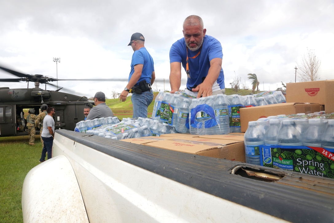 Soldiers work with the locals to unload food and water from a HH-60M Black Hawk helicopter into trucks to be distributed to residents within the city in Orocovis.