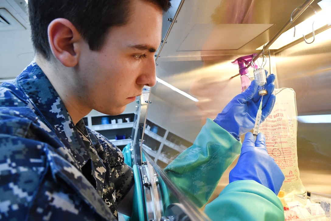 Navy Seaman Jesse Kemper mixes medication in an isolation hood aboard the hospital ship USNS Comfort.