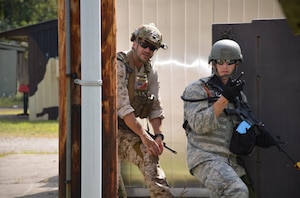 Two people in military uniform carry guns during an exercise.