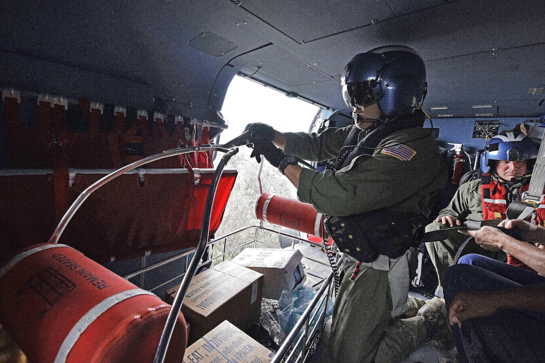Petty Officer 3rd Class Ron Carrasquillo prepares a basket of relief supplies to lower from a Coast Guard MH-65 Jayhawk helicopter to victims.