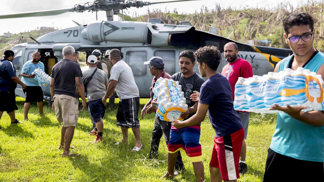 Sailors and volunteers unload bottled water from a helicopter