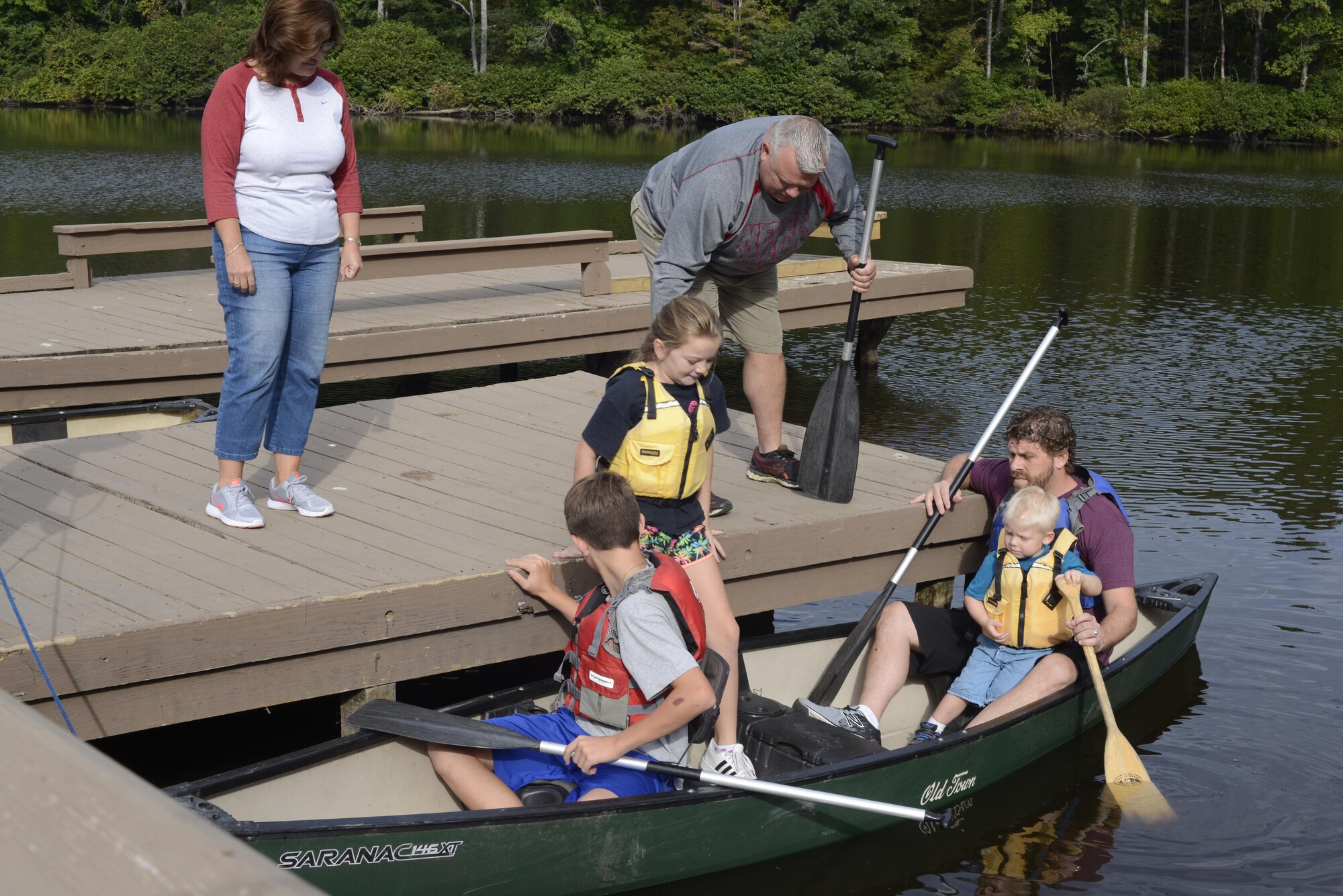 A female and a male on a dock help four people get into a canoe for them to explore the lake.