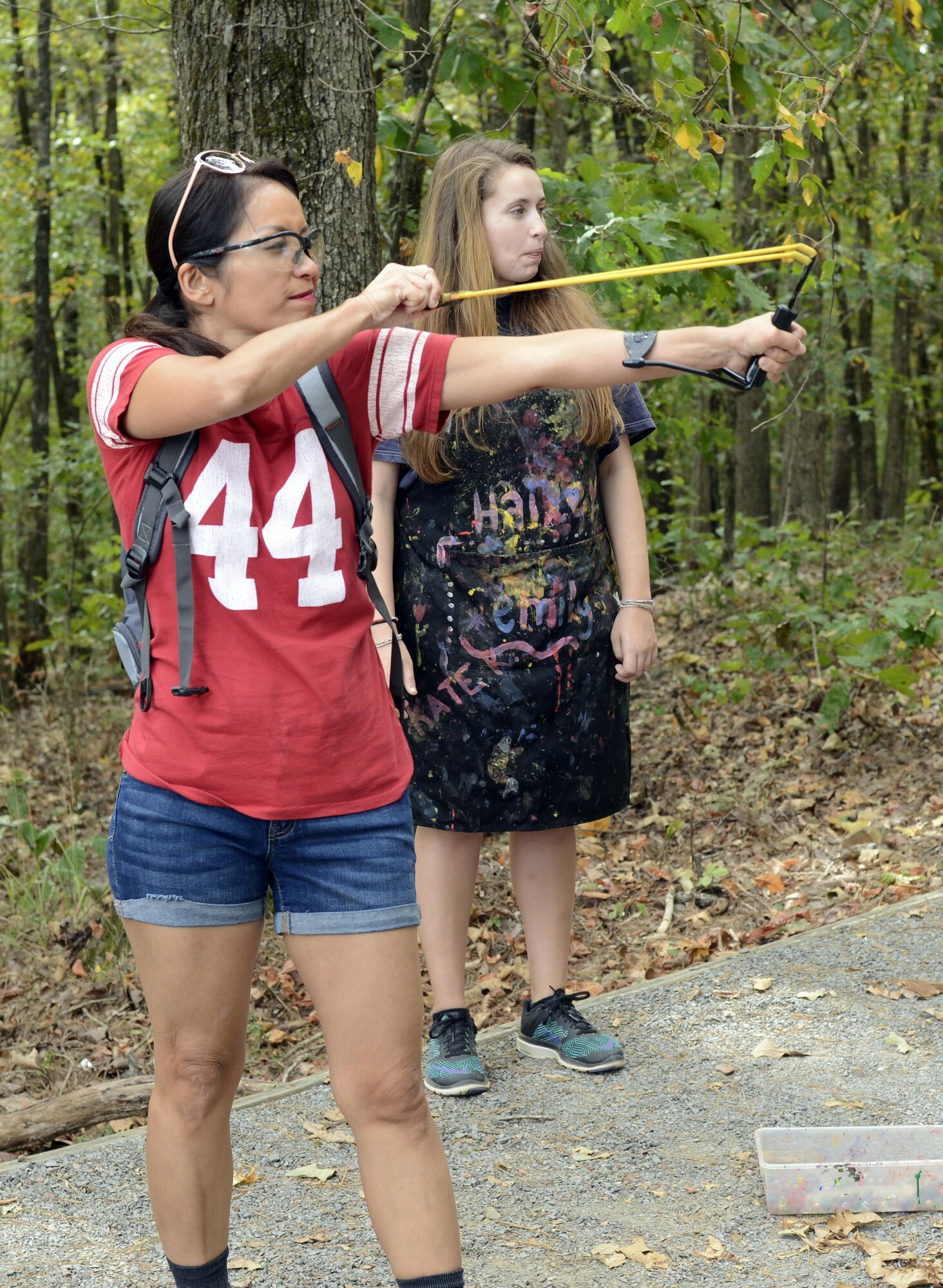 A woman fires a slingshot as another woman watches behind her.