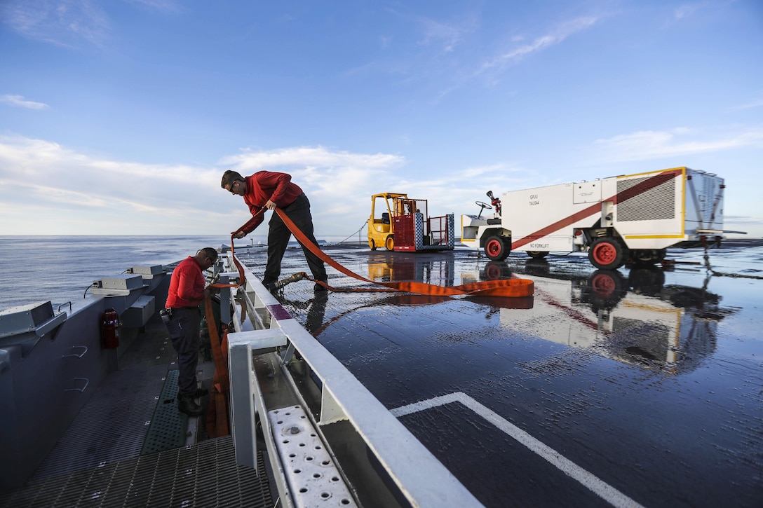 Sailors put away firefighting equipment on a ship's flight deck.