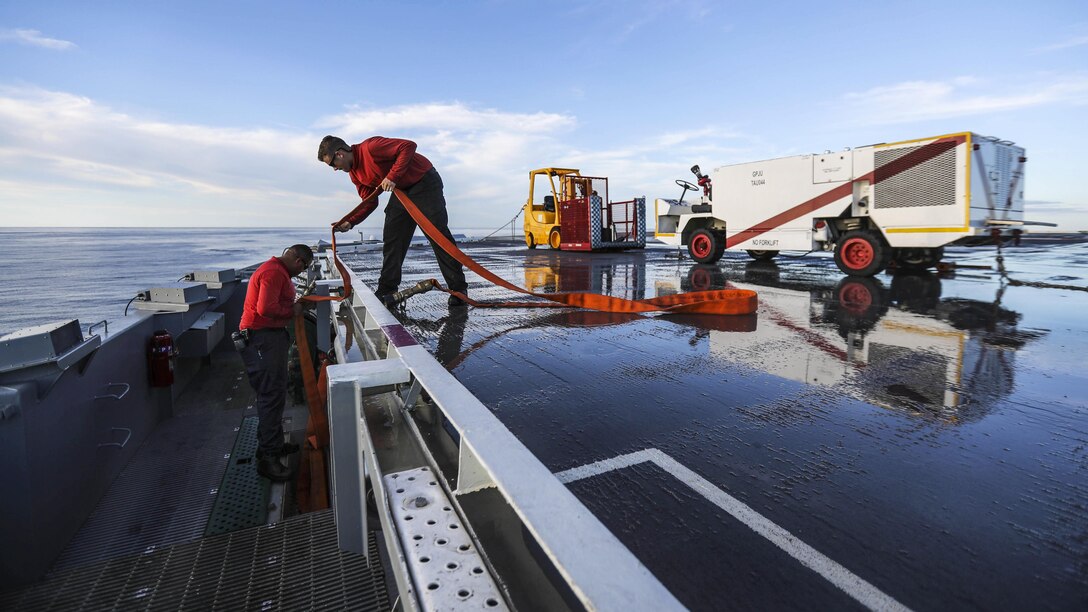 Sailors put away firefighting equipment on a ship's flight deck.