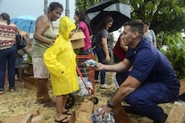 A service member hands a child in a yellow coat some food.