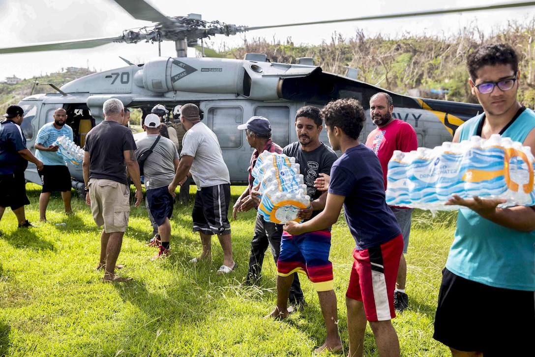 Sailors and volunteers unload bottled water from a helicopter