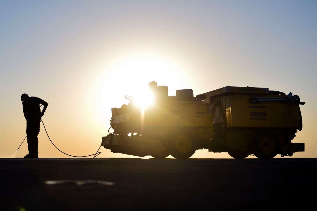 Two airmen clean the flight deck of a ship.