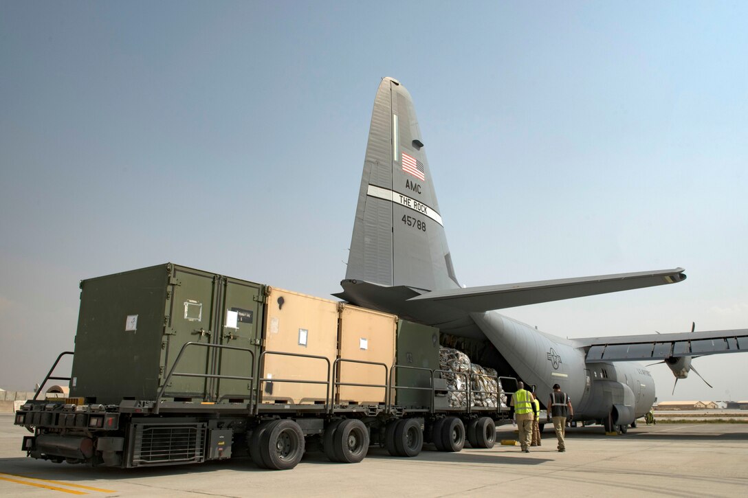 Airmen and contractors load cargo onto a C-130J Super Hercules aircraft.