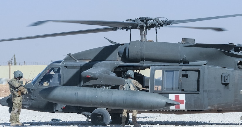 Pilots and crew chiefs stand outside a helicopter.