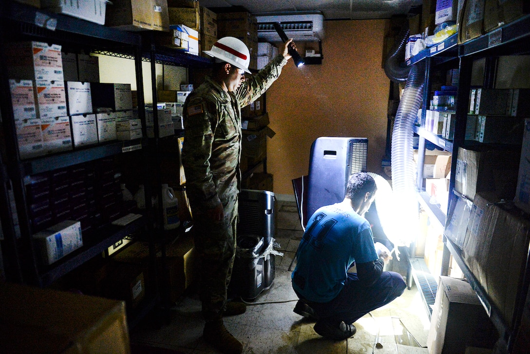 Army Spc. Richard Alicea, left, shines a flashlight helping Angel Rodriquez, a volunteer, fix an air conditioning tube.