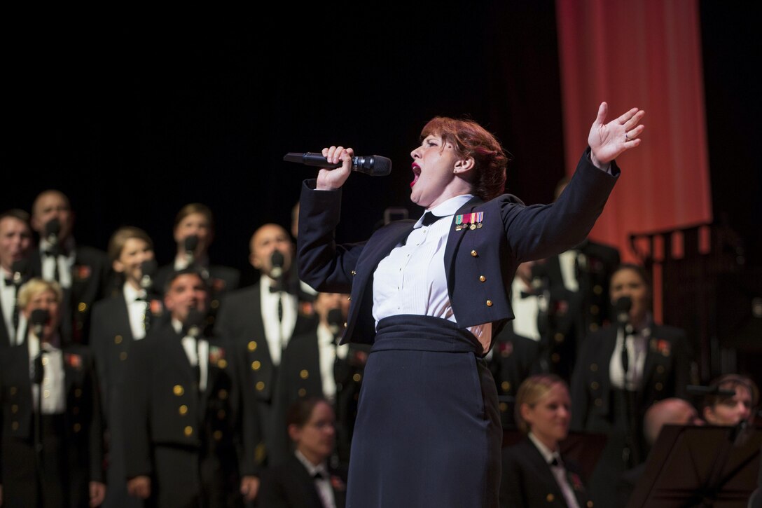 A raises one arm while singing in front of a group of musicians.