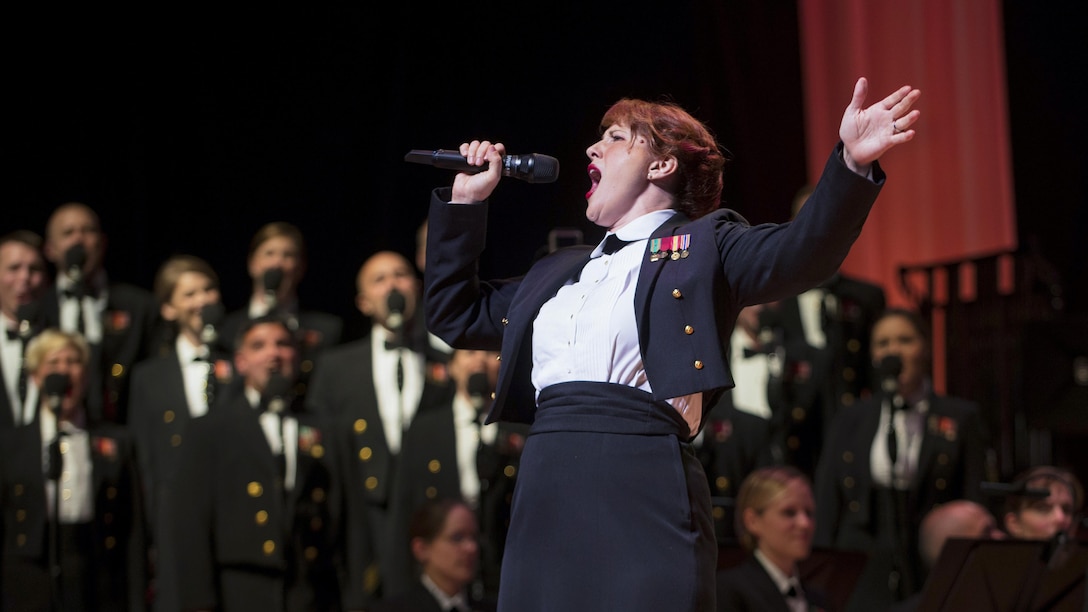 A raises one arm while singing in front of a group of musicians.