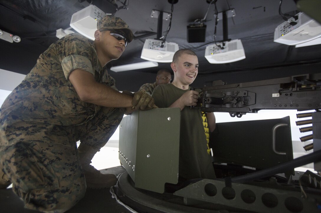 Pfc. Manuel Nava, a machine gunner with 2nd Battalion, 3rd Marine Regiment, watches Maddox Hyde fire the mounted .50-caliber machine gun simulator during a tour of Marine Corps Base Hawaii, (MCBH) Sept. 27, 2017. The Hyde family was led on tours of Marine Corps Air Station Kaneohe Bay, ARFF, and took part in various simulators across MCBH as part of Maddox’s wish to see where his father served before he begins his next cycle of cancer treatment. (U.S. Marine Corps photo by Lance Cpl. Luke Kuennen)