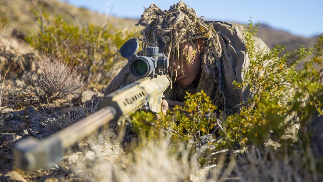 A Marine on the ground looks through a weapon scope.