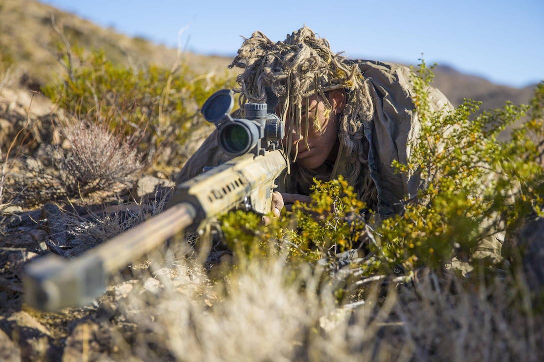 A Marine on the ground looks through a weapon scope.