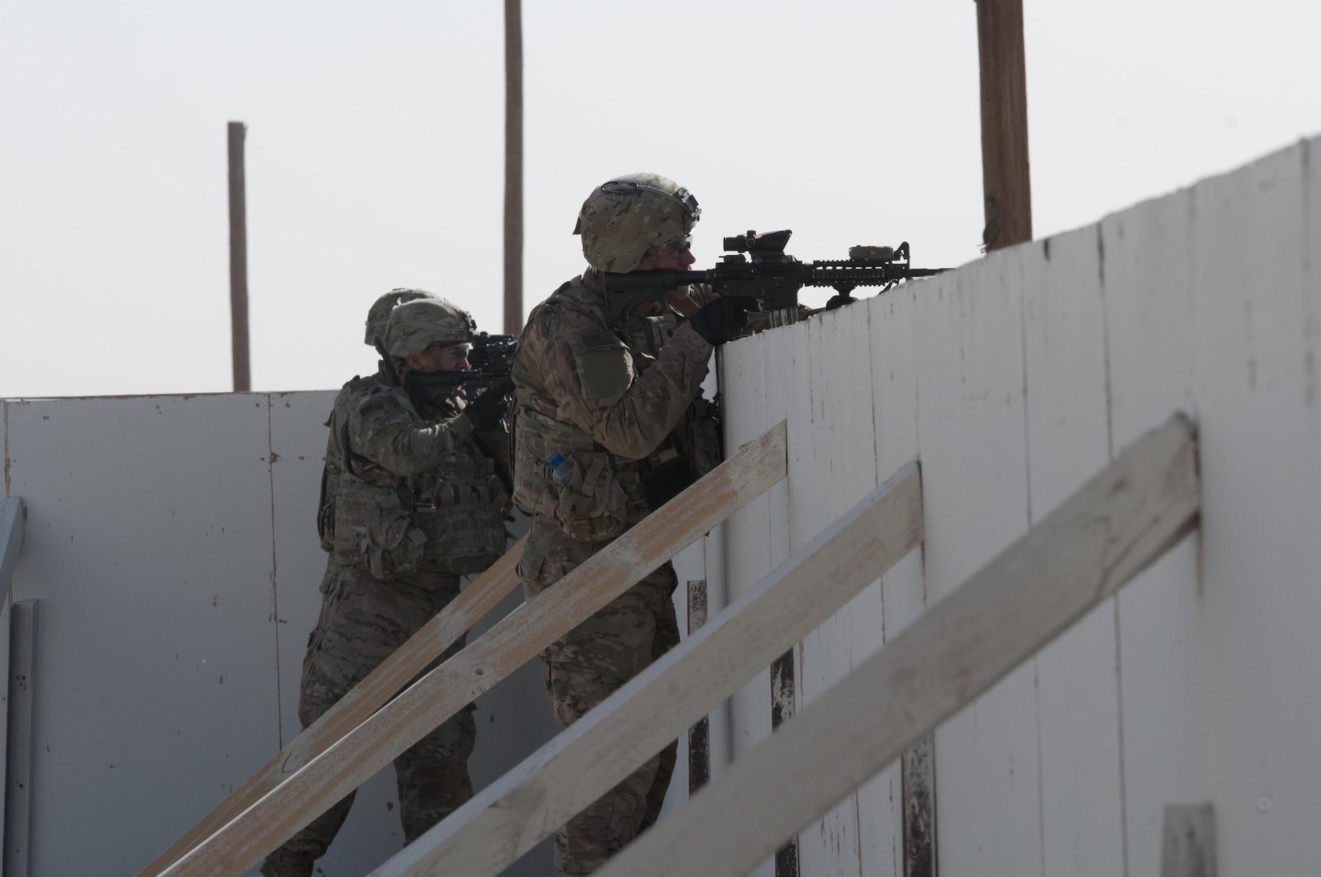 Two soldiers aim their weapons over a wall.