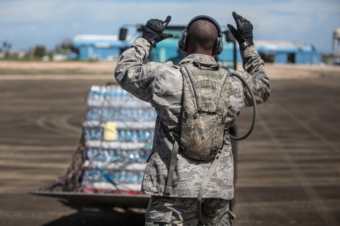 An airman uses hand signals while directing a forklift operator offloading pallets of water from a 727 commercial airliner.