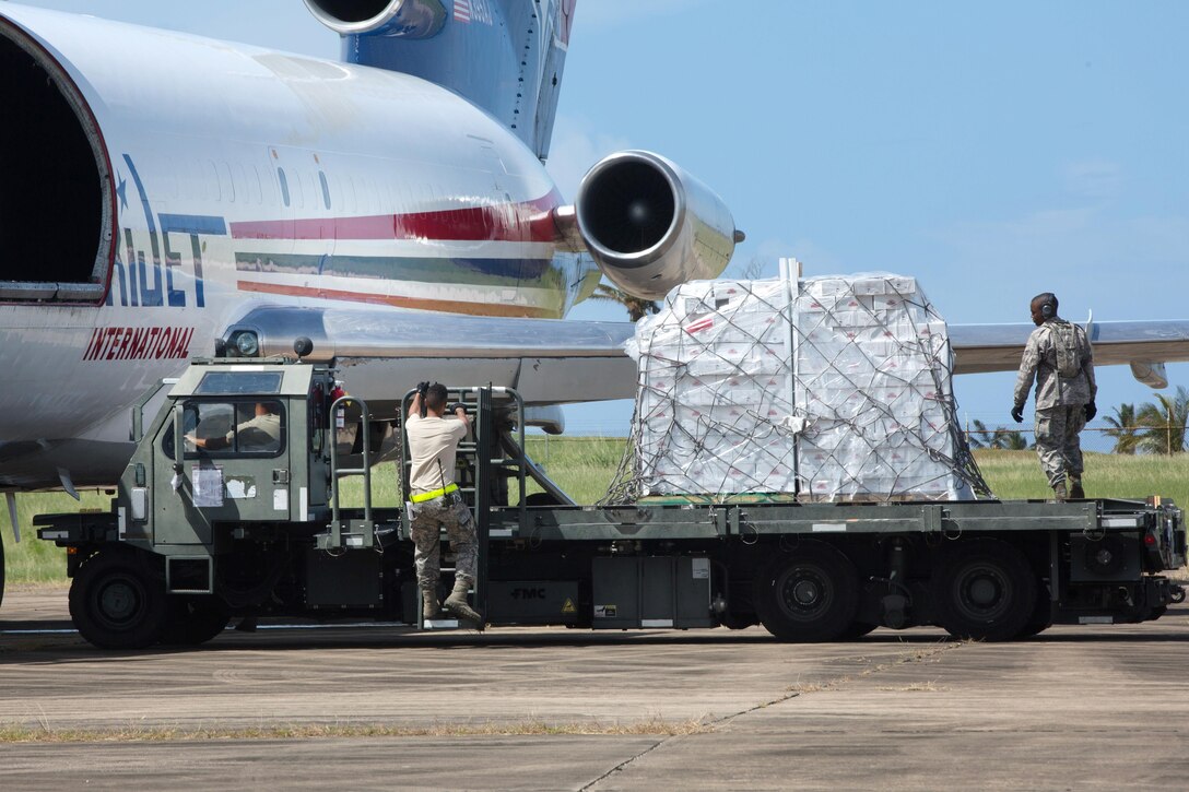 Airmen unload pallets of food from a 727 commercial airliner onto a K-loader.