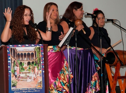 IMAGE: DAHLGREN, Va. (Sept. 28, 2017) - Isha Renta, a National Oceanic and Atmospheric Administration meteorologist, sings as music is played by Semilla Cultural (Cultural Seed) volunteers at the Naval Surface Warfare Center Dahlgren Division (NSWCDD) sponsored Hispanic Heritage Observance. The performers on stage are NSWCDD scientists and engineers. Renta founded the Semilla Cultural nonprofit organization to cultivate a community that embraces diversity by educating, promoting and disseminating Puerto Rican culture and traditions. The Bomba is a dialogue between the primo drummer and the dancer where the dancer dictates the rhythm of the percussion and the drummer follows the dancer's body and skirt movements. The primo drummer improvises as the dancer challenges the drummer to follow the dancer's improvised movements, called piquetes. Bomba singing is based on a call-response structure in which the lead singer begins the song and is answered by a melody sung by the chorus.