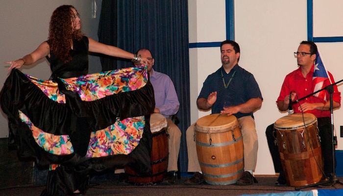 IMAGE: DAHLGREN, Va. (Sept. 28, 2017) - Isha Renta, a National Oceanic and Atmospheric Administration meteorologist, dances to Bomba music played by Semilla Cultural (Cultural Seed) volunteers at the Naval Surface Warfare Center Dahlgren Division (NSWCDD) sponsored Hispanic Heritage Observance. The performers on stage are NSWCDD scientists and engineers. Renta founded the Semilla Cultural nonprofit organization to cultivate a community that embraces diversity by educating, promoting and disseminating Puerto Rican culture and traditions. The Bomba is a dialogue between the primo drummer and the dancer where the dancer dictates the rhythm of the percussion and the drummer follows the dancer's body and skirt movements. The primo drummer improvises as the dancer challenges the drummer to follow the dancer's improvised movements, called piquetes. Bomba singing is based on a call-response structure in which the lead singer begins the song and is answered by a melody sung by the chorus.