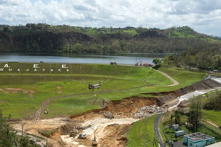 A CH-47 Chinook helicopter prepares to emplace large sand bags to fortify the spillway of the Guajataca Dam.