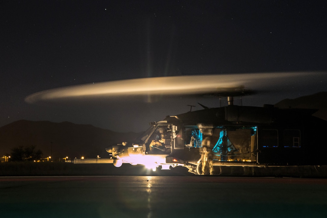 A helicopter sits on the ground with the blades still rotating.