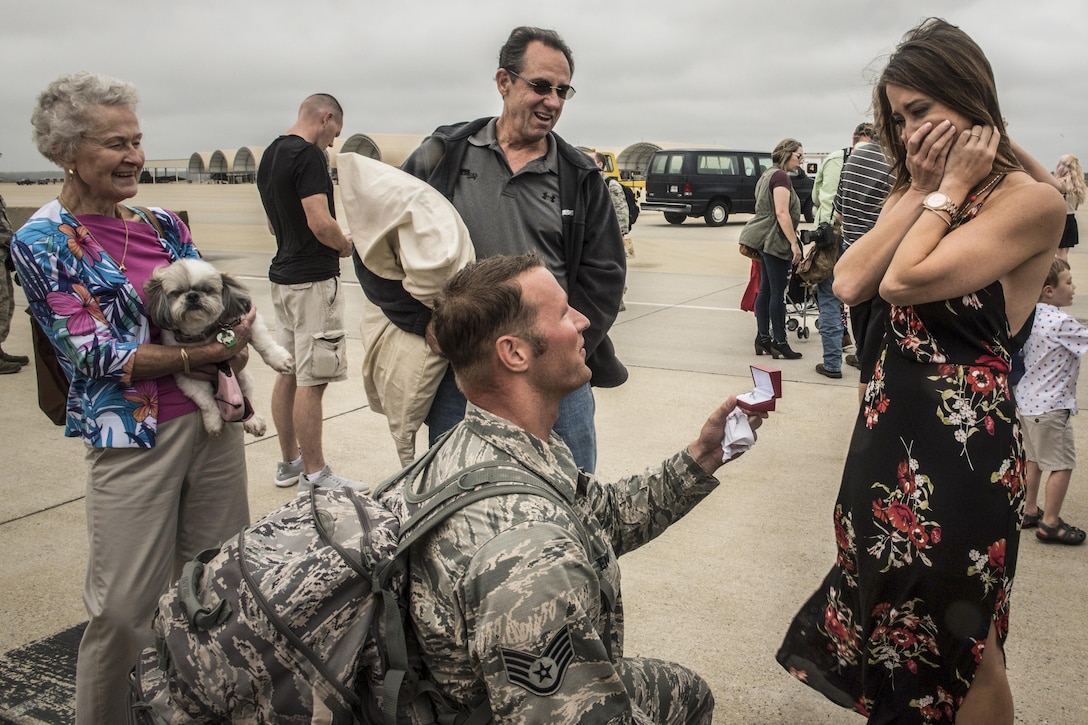 An airman kneels to proposed to his girlfriend at a base.