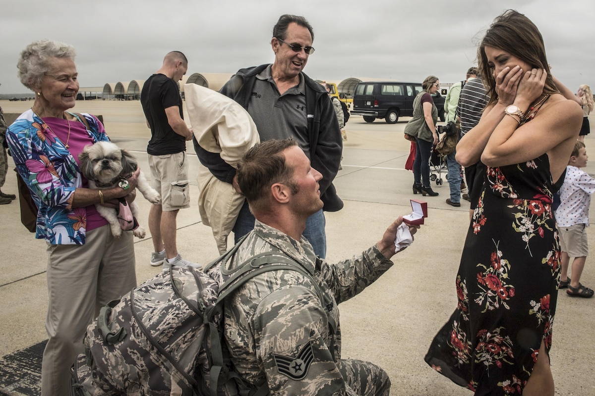 An airman kneels to proposed to his girlfriend at a base.