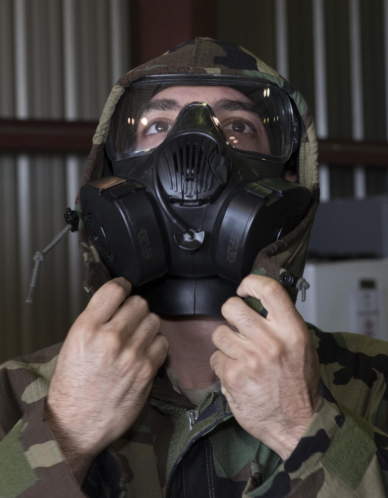 A U.S. Air Force Airman pulls the hood of his mission-oriented protective posture jacket closed over his gas mask to ensure a proper seal during a chemical, biological, radiological and nuclear defense survival skills training course at Travis Air Force Base, Calif., Sep. 21, 2017. Airmen are refreshed on vital skills that may save their lives while on duty by learning proper ways to put on protective equipment in a timely and efficient manner. (U.S. Air Force photo by Heide Couch)