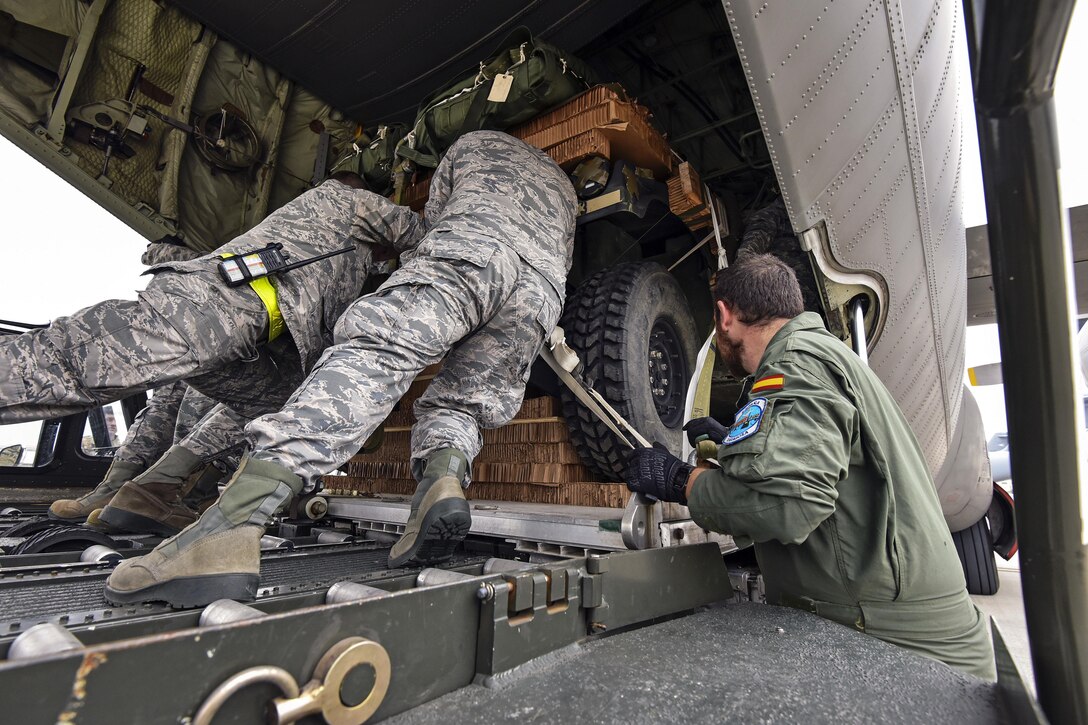 Two U.S. service members push a vehicle into place on an airplane.