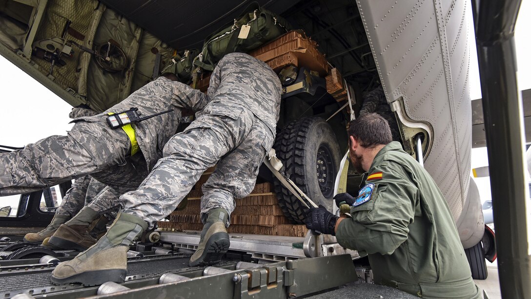 U.S. service members push a vehicle into place on an airplane.