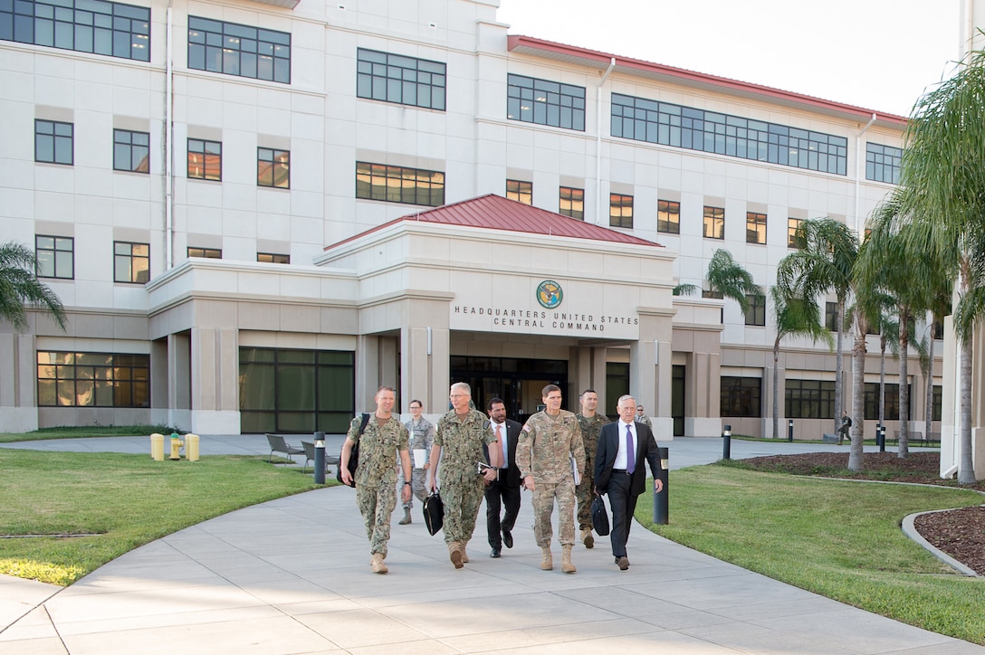 Defense Secretary Jim Mattis walks with service members outside a building.