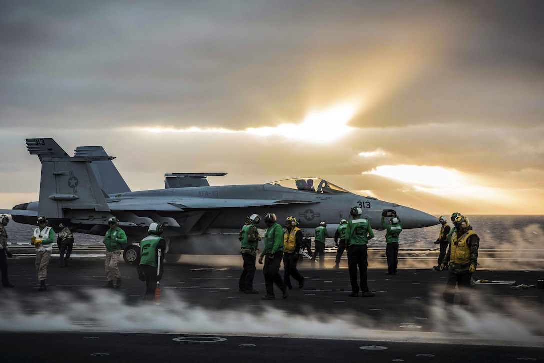 Sailors prep an aircraft on a ship's flight deck.