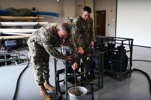Two sailors operate a machine.