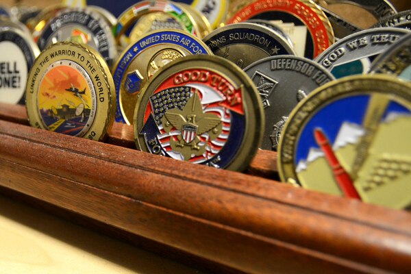 Rows of challenge coins sit in a wooded holder.