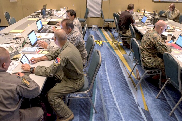 Lines of people and service members sit at tables and look at papers and laptops.