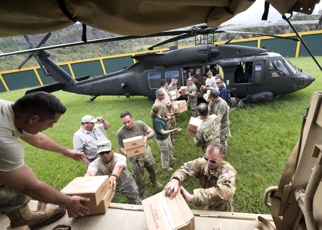 Two lines of people unload boxes from a helicopter.