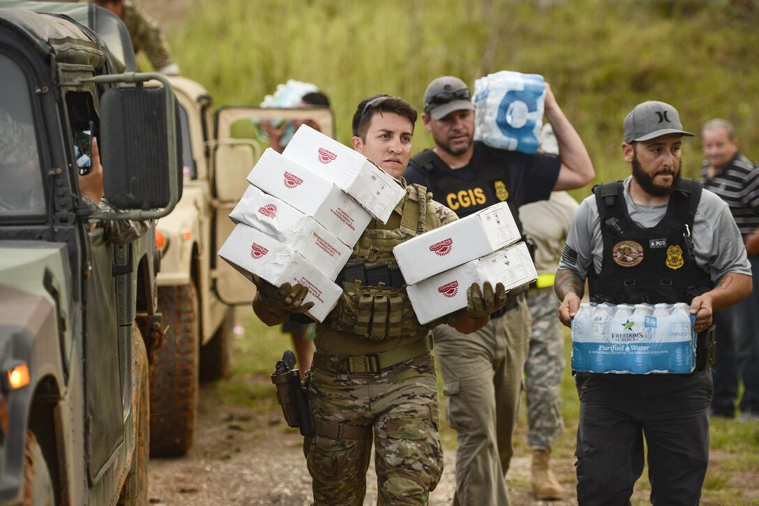 A group of people carry cases of water and boxes.