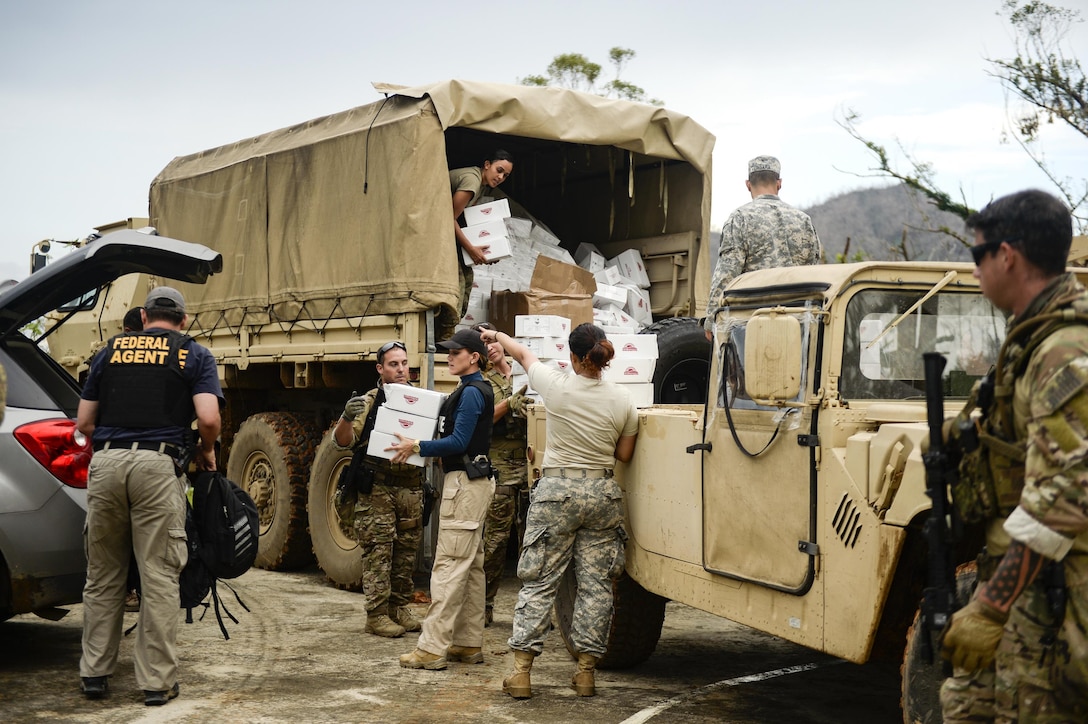 A group of people unload boxes from the back of a military vehicle.