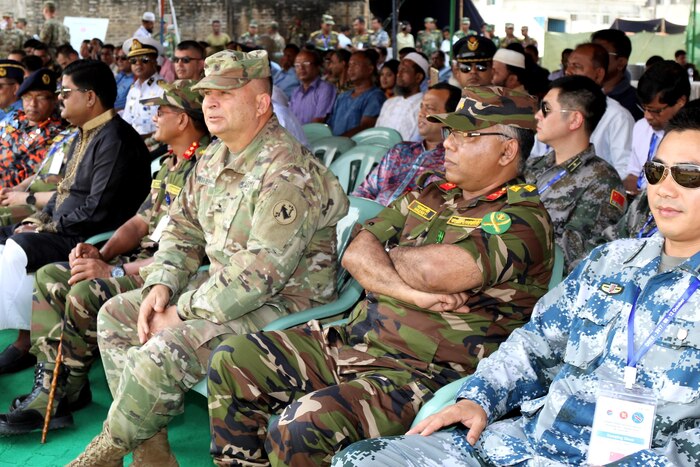 An audience of seated military members and civilians look forward.