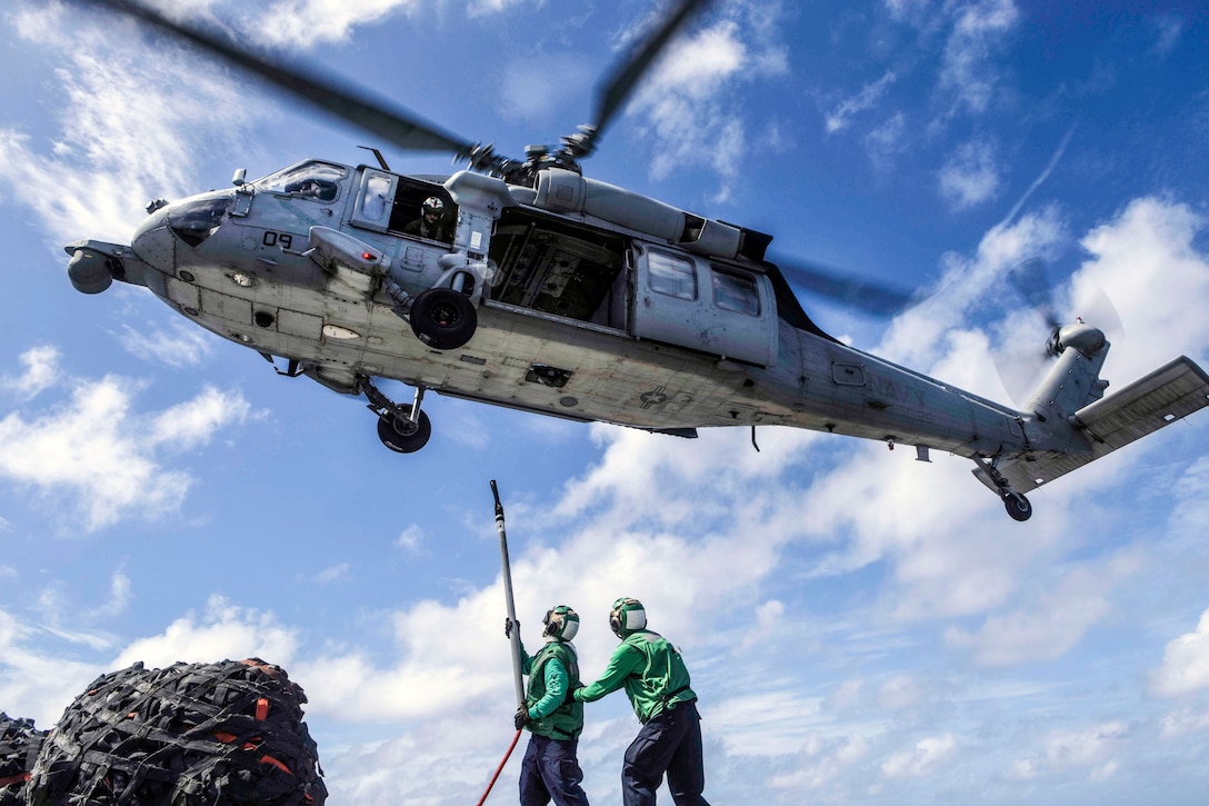 Two sailors reach a line and hook up toward a hovering helicopter.