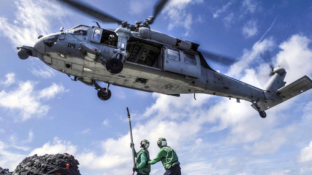 Two sailors reach a line and hook up toward a hovering helicopter.