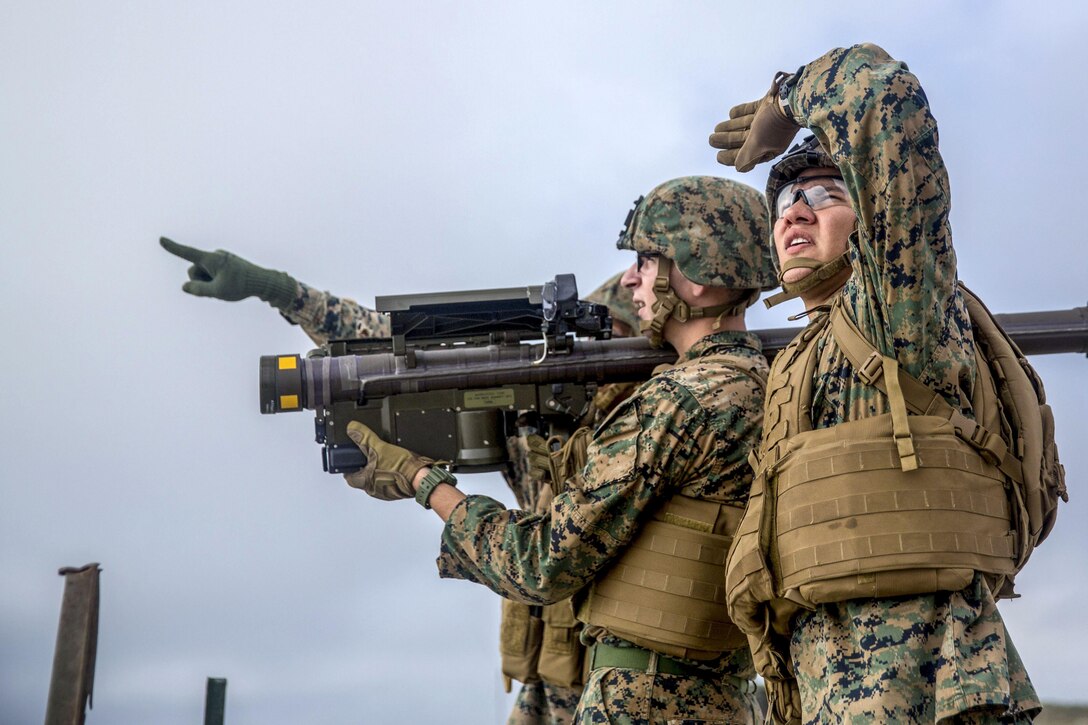A Marine looks up and shades his eyes while another holds a weapon and a third points.