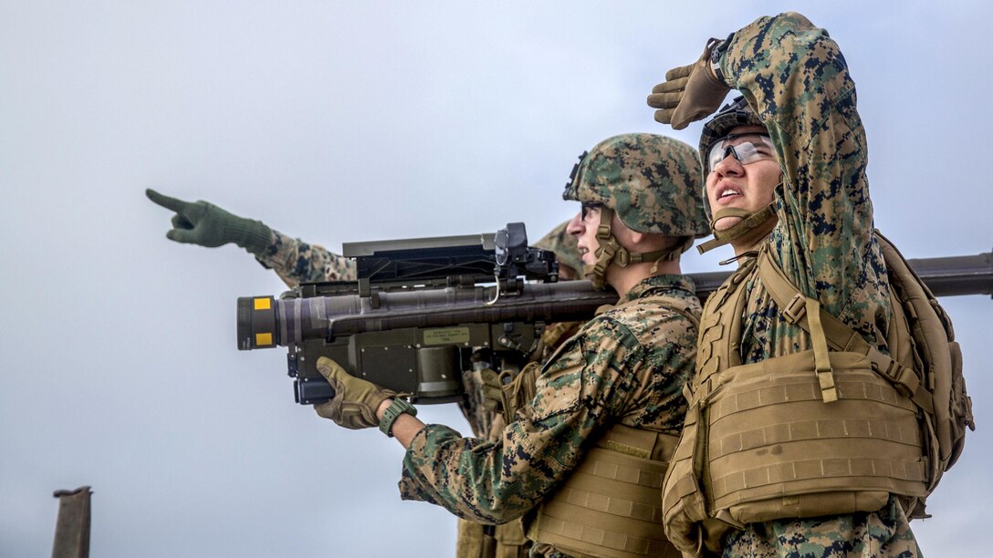 A Marine looks up and shades his eyes while another holds a weapon and a third points.